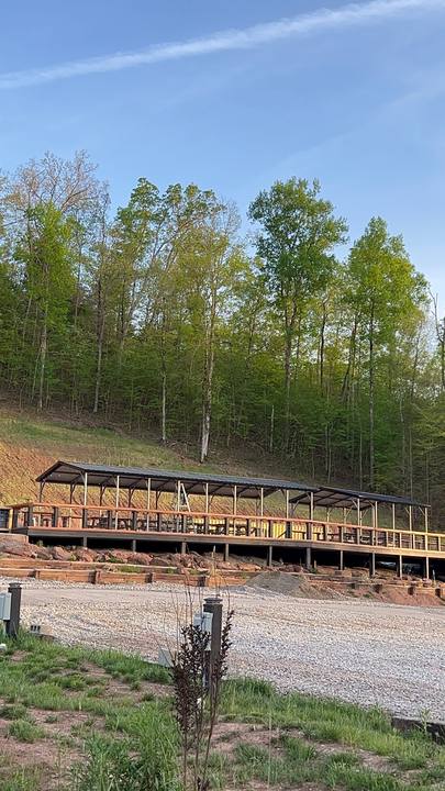 A long covered deck below a wooded hillside, gravel lot in front