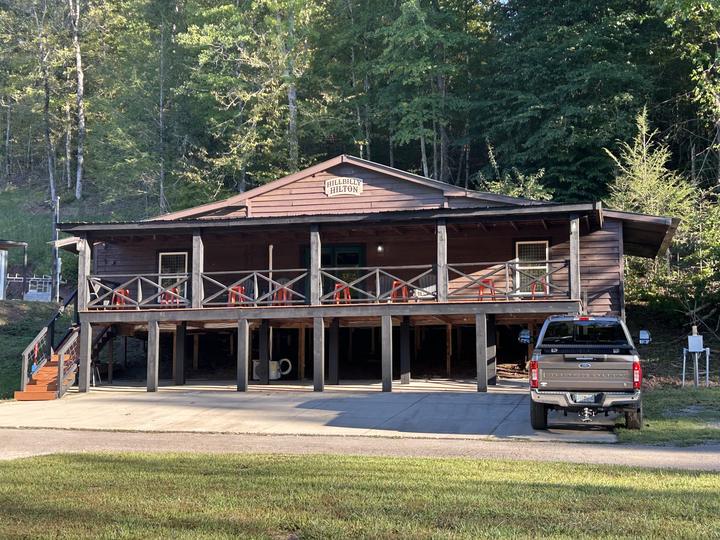 The Hillbilly Hilton, a long two-story wooden building with a covered porch, seen across the lawn