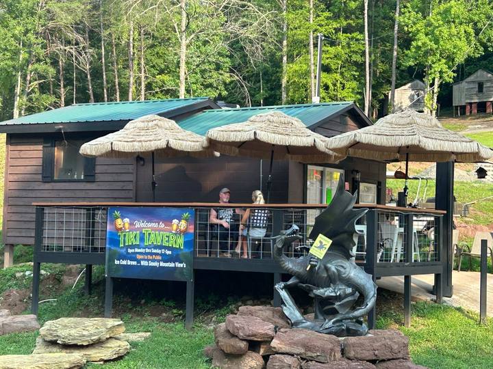 Guests on a deck under thatched umbrellas, the dragon statue on rocks out front