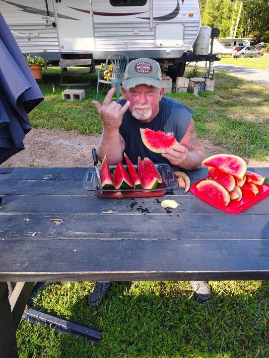 A guest at a picnic table with fresh-cut watermelon, campers parked behind